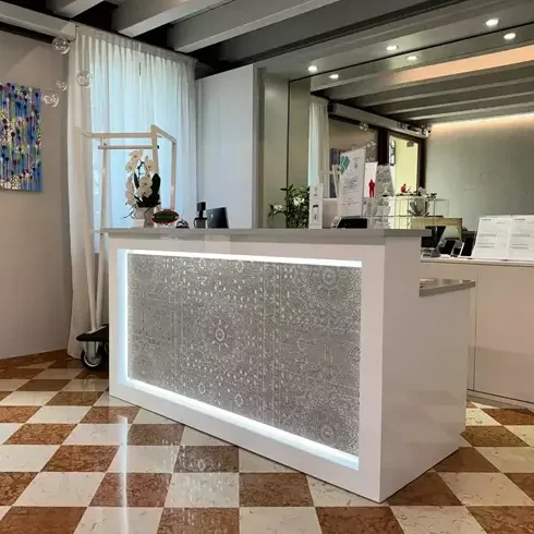 Dettaglio del banco reception in legno chiaro, inserito in un ambiente luminoso e accogliente