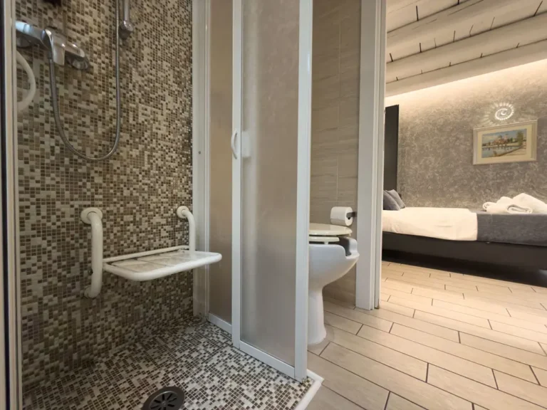 Dettaglio del bagno accessibile dell'Albergo Fontana a Verona, dotato di maniglioni di sicurezza, doccia a filo pavimento e ampi spazi di manovra per garantire comfort e autonomia.